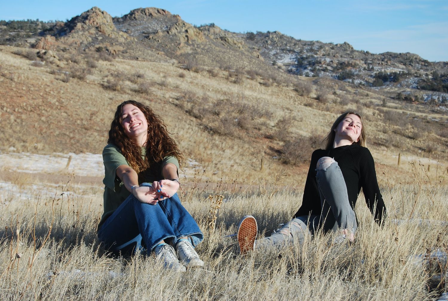 People relaxing in golden grass with rocky mountain backdrop on sunny day.