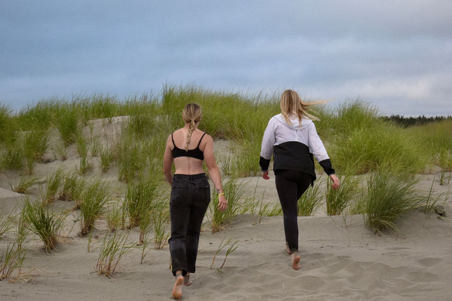 Two people walking through beach grass on sandy dunes at dusk.