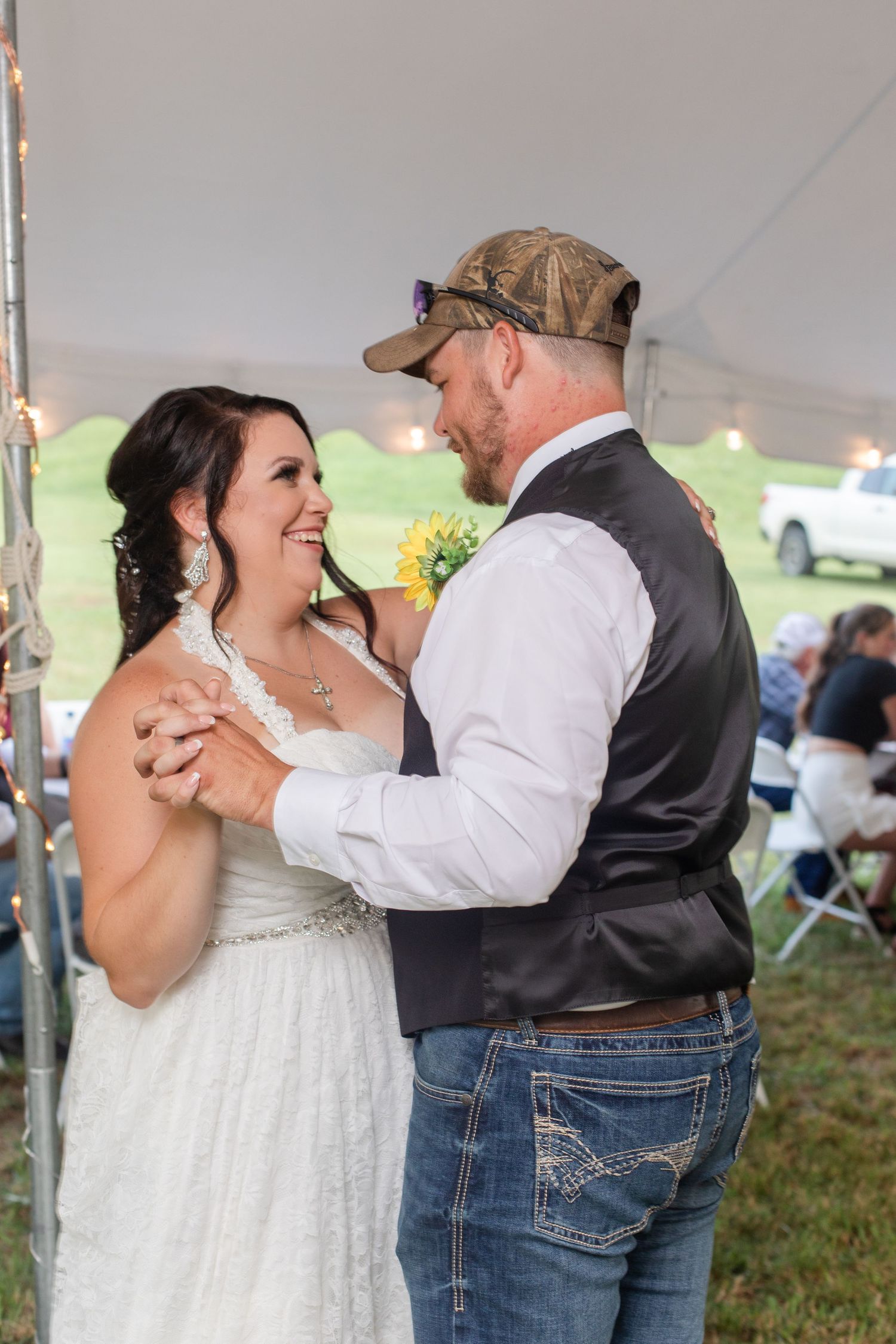 Newlyweds dancing and laughing together under a reception tent.