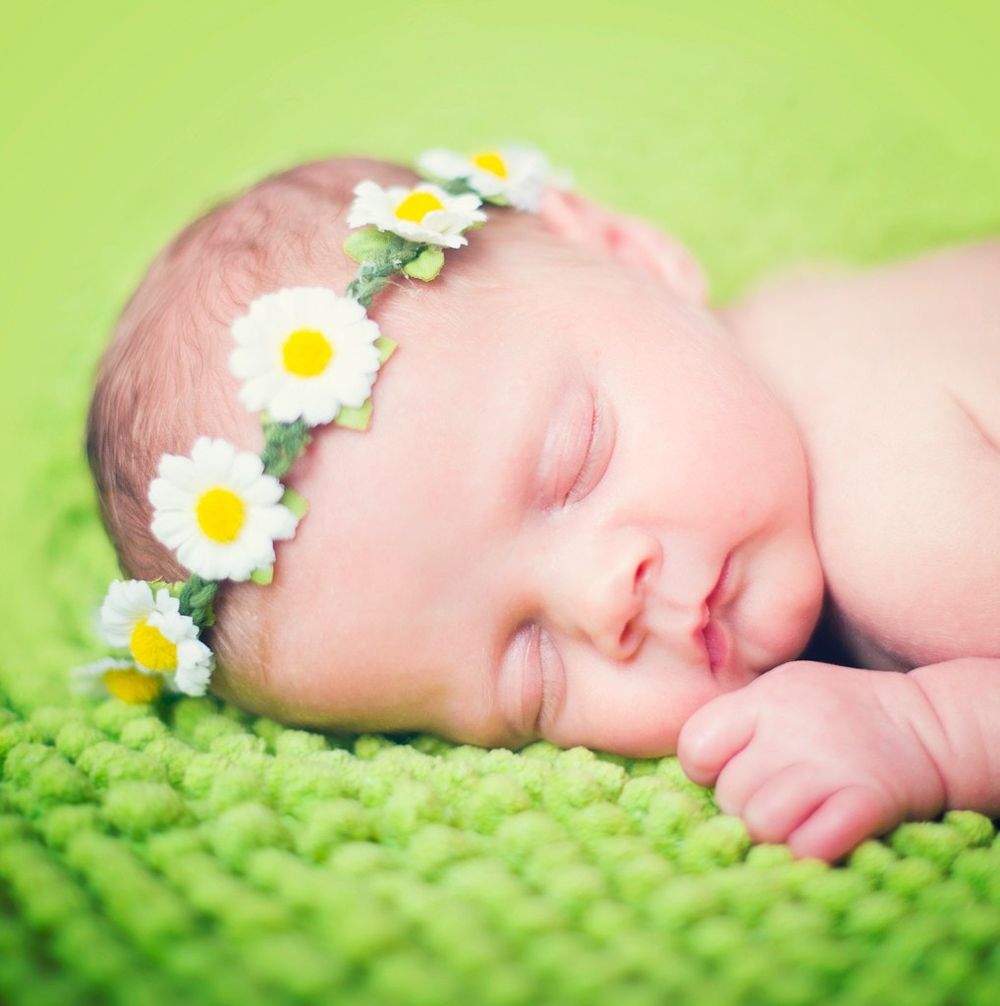 Sleeping newborn wearing daisy flower crown on green textured blanket.