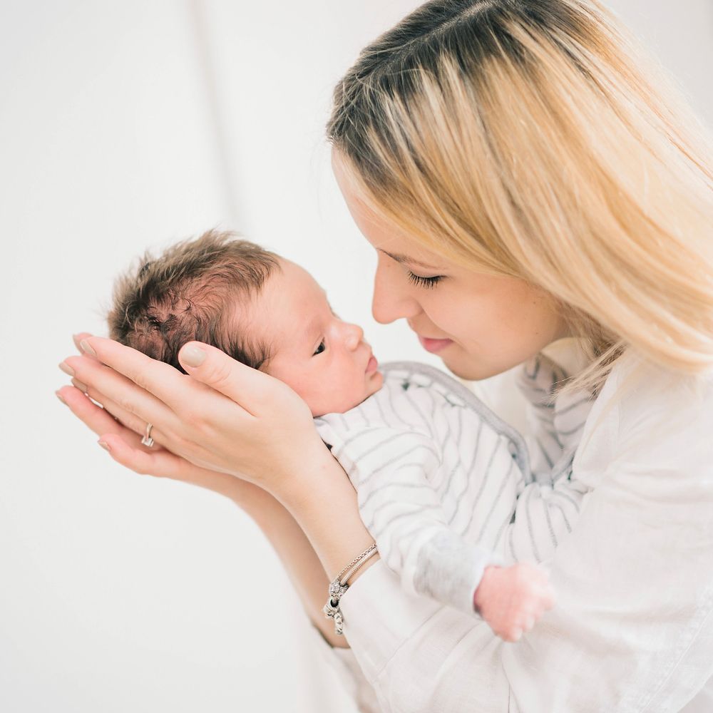 Tender moment between parent and newborn baby in soft white setting.