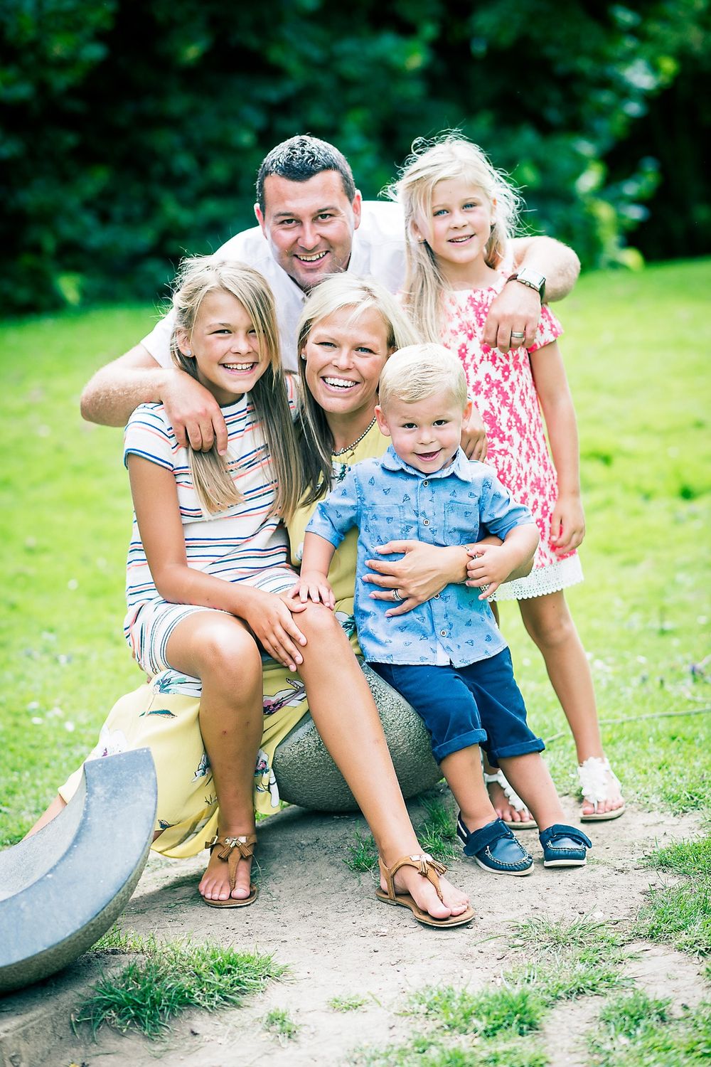Happy family poses together on playground equipment outdoors on sunny day.