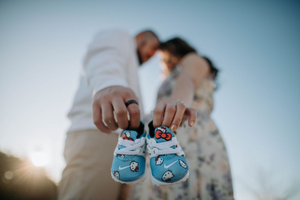 A pair of blue baby shoes held up against a sunset sky in a pregnancy announcement photo.