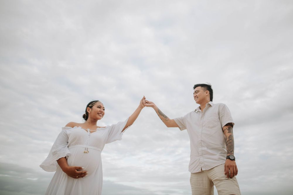 A couple in light-colored attire shares a celebratory high-five against a cloudy sky on the beach.