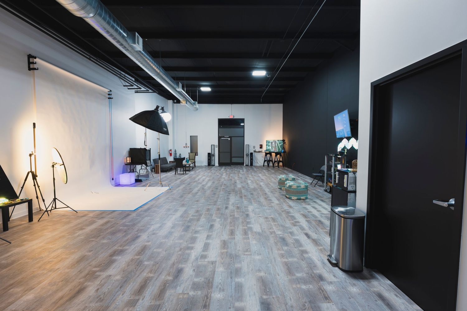 Large photography studio space with gray flooring, white walls and professional lighting setup.