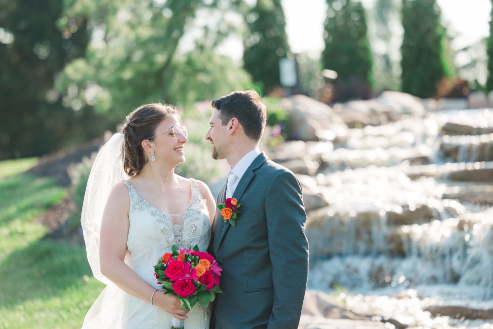 Intimate wedding moment captured by stone waterfall with bright pink bouquet and formal attire.