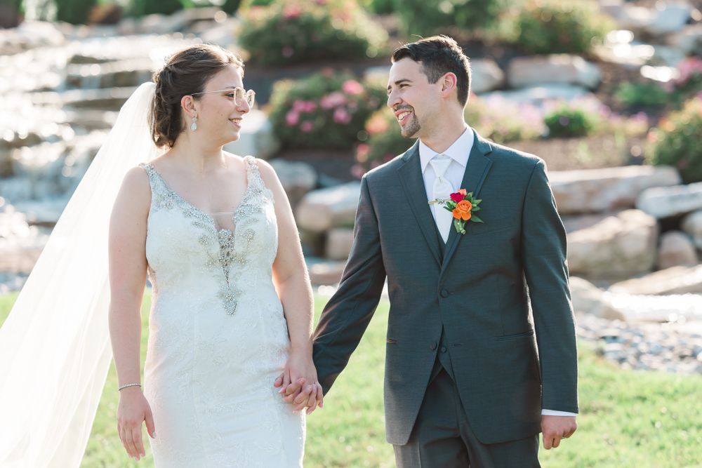 Newlyweds share intimate moment on grassy hill with stone landscaping in background.