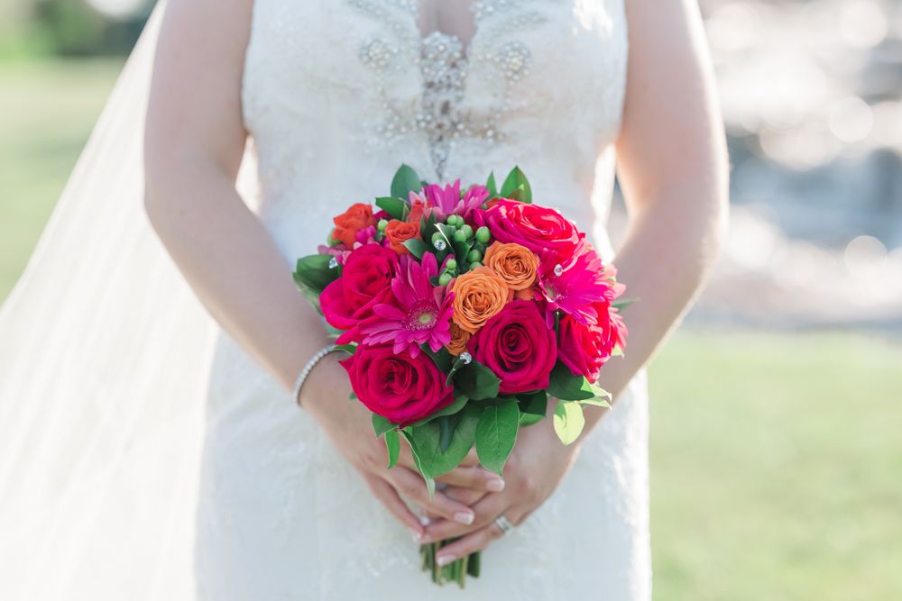 Close up of bright pink and red rose wedding bouquet held against white lace dress.