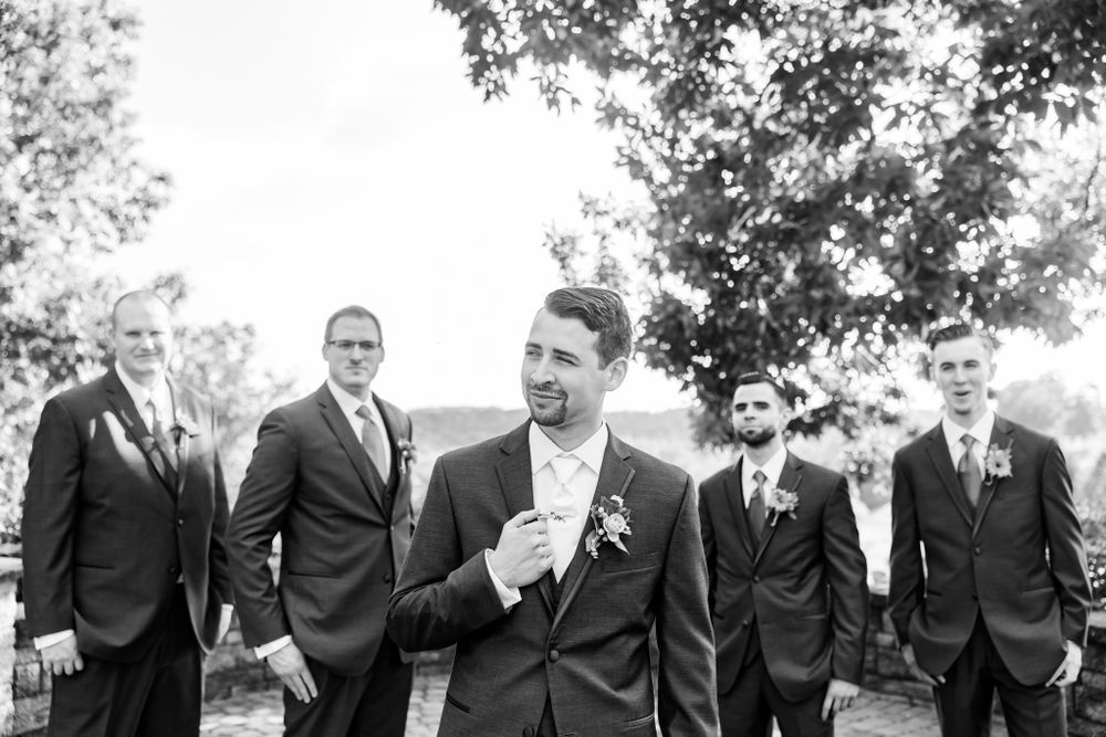 Groomsmen in formal attire gather for a black and white portrait outdoors.