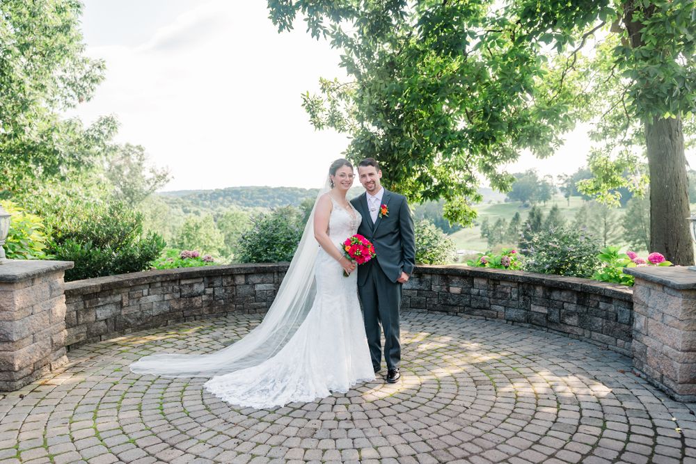 Wedding couple stands on circular stone patio with lush greenery and scenic mountain backdrop.