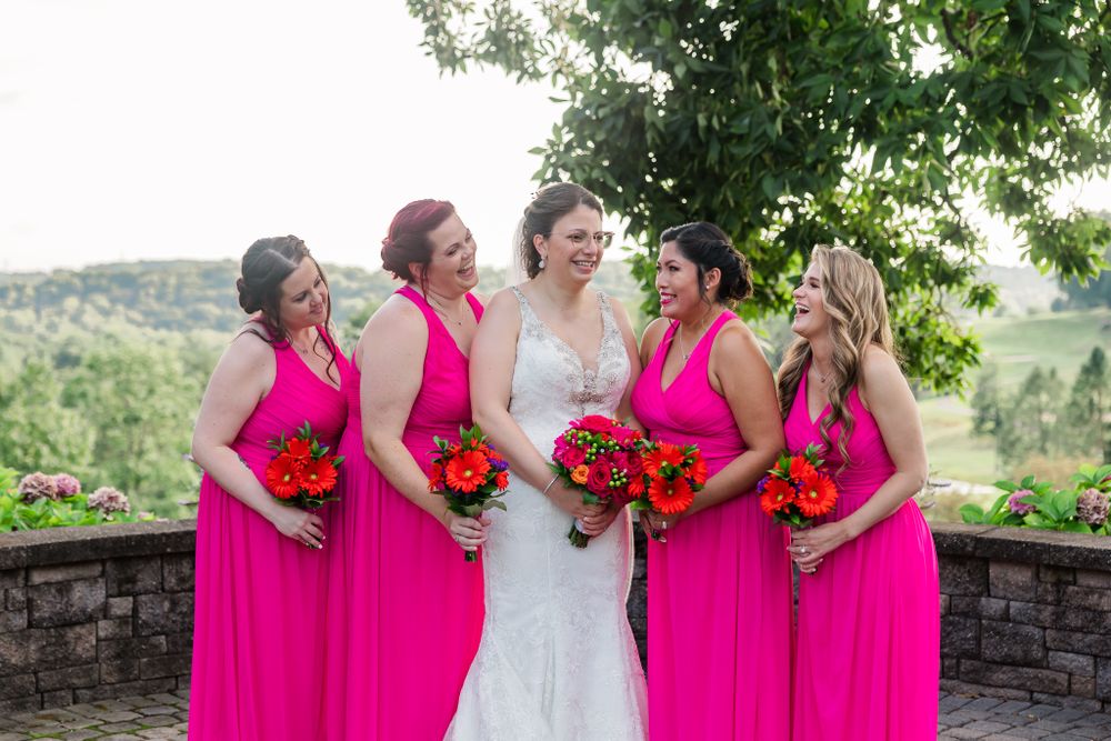 Wedding party poses outdoors wearing bright pink dresses and holding vibrant red bouquets.