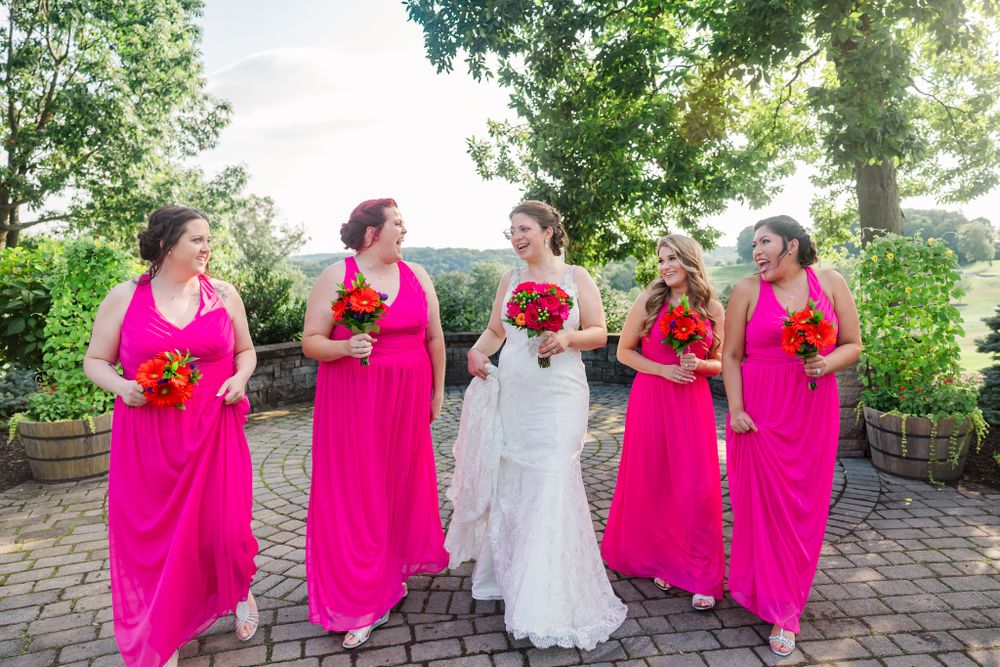 A bridal party in hot pink dresses poses together on stone patio with red bouquets.