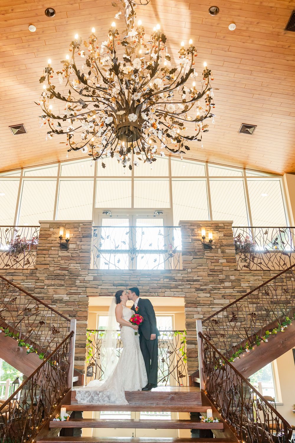An elegant grand staircase with iron railings and a stunning crystal chandelier in a wedding venue.