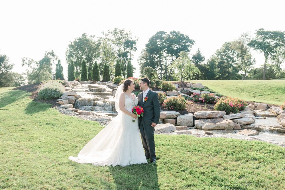 Sunlit wedding portrait on landscaped lawn with cascading stone waterfall in background.