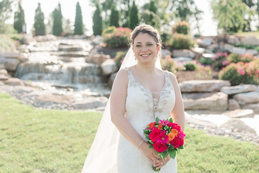 Outdoor bridal portrait featuring lace dress and bright pink bouquet against stone waterfall backdrop.