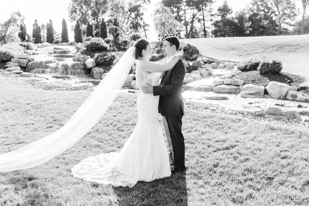 Black and white wedding photo of couple dancing on lawn with flowing veil and rock landscaping.
