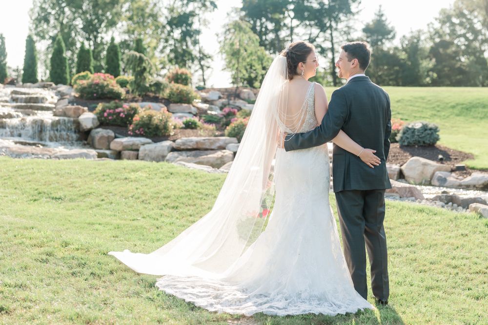 Romantic wedding photo showing couple embracing on lawn with landscaped rock waterfall behind them.