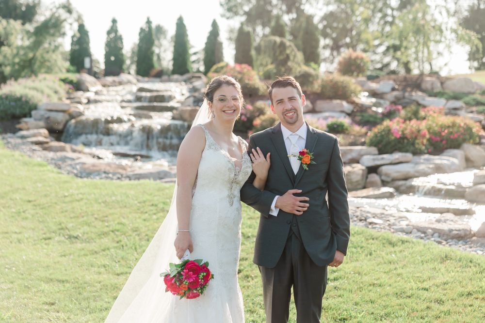 Newlyweds pose on grass with cascading rock waterfall feature in background.