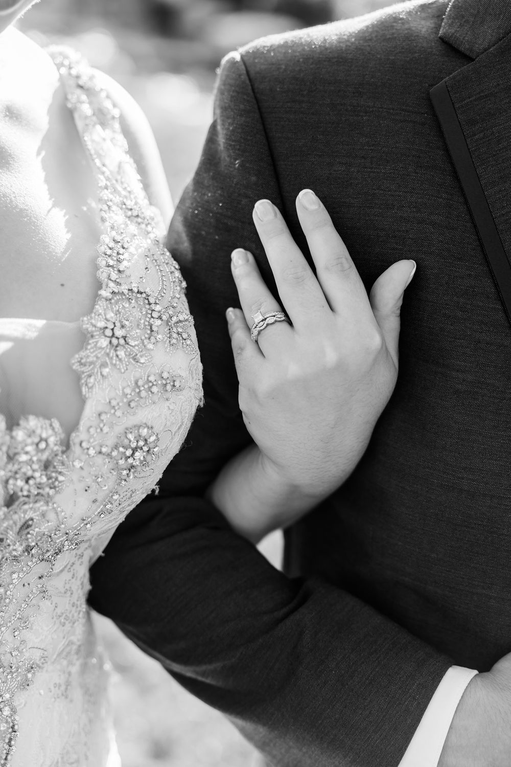 Close-up black and white photo of wedding ring and lace dress detail.