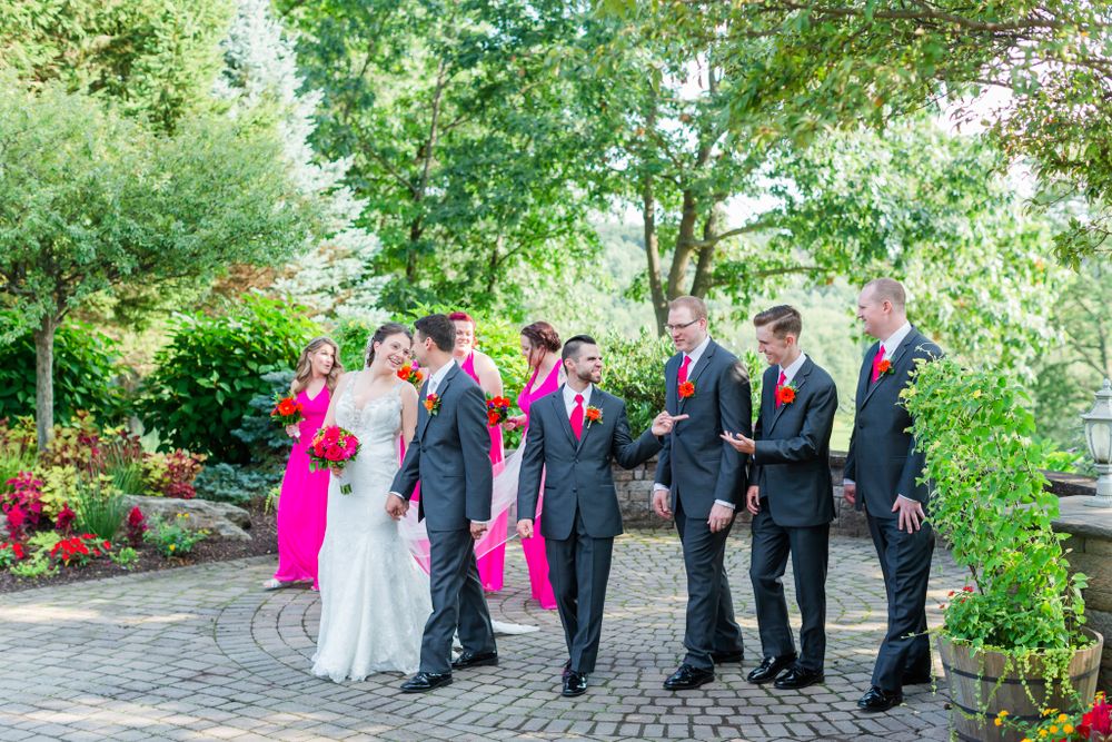 Wedding party gathers on circular brick patio with bright pink accents and floral decorations.