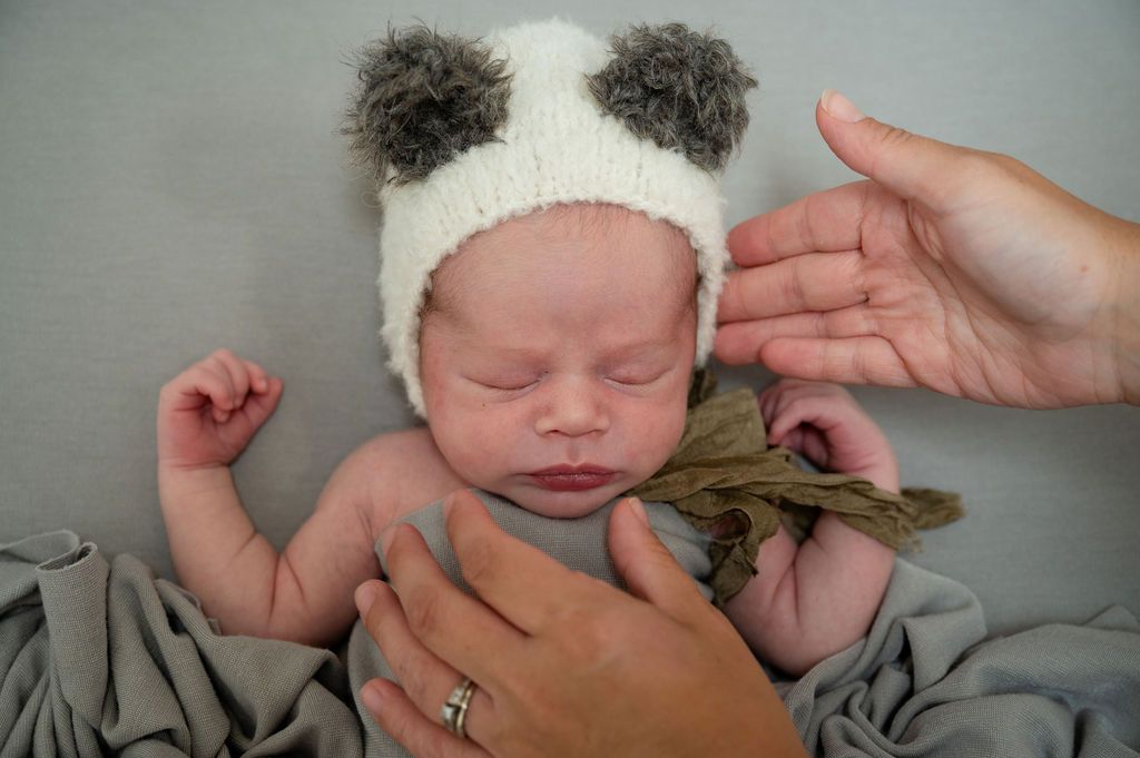 Newborn wearing panda bear hat lying peacefully on gray blanket.