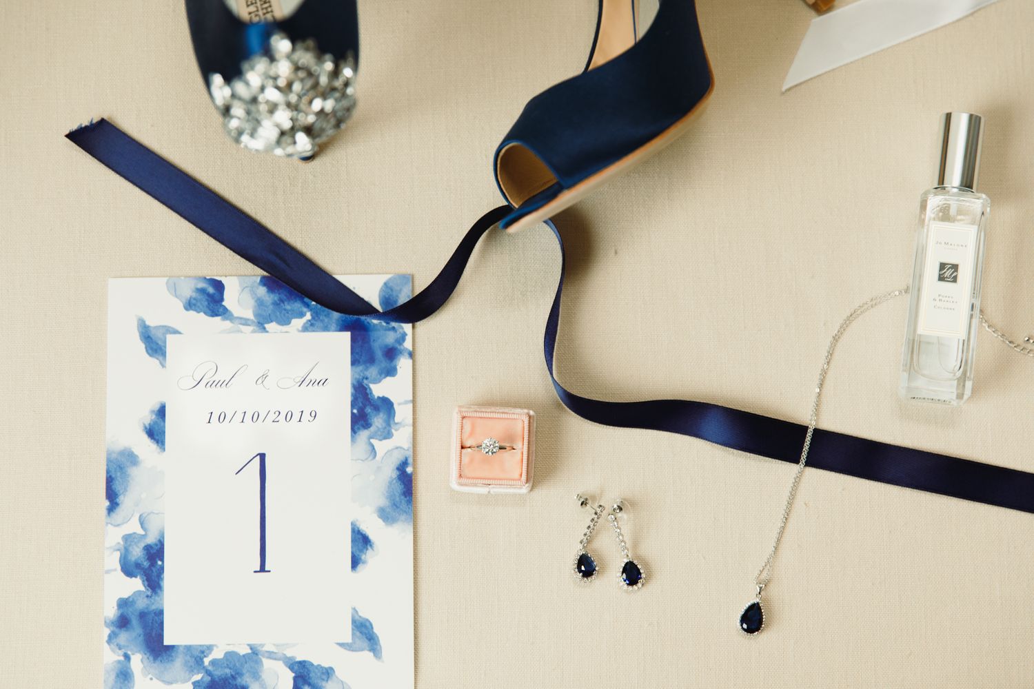 Wedding details flatlay with blue ribbon, table number, jewelry and perfume.
