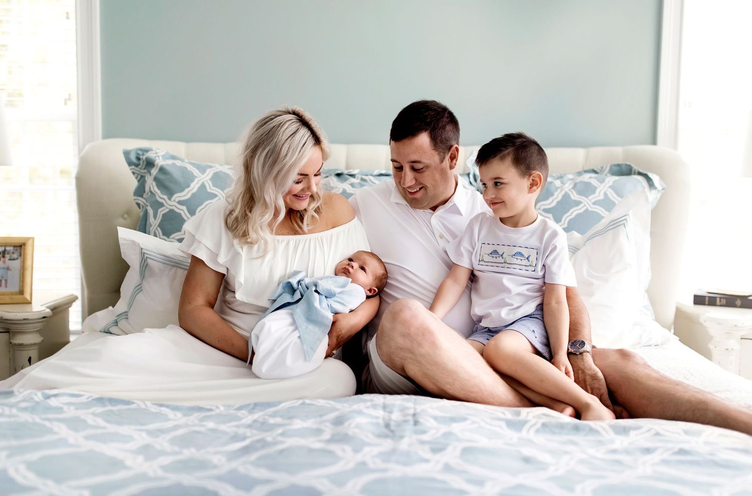 A loving family moment on a cozy bed with patterns of blue and gray as they bond with their newborn.