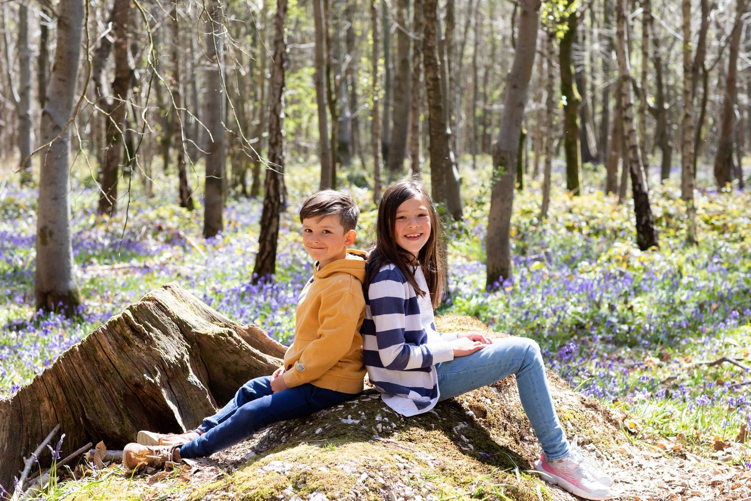 Friends relaxing on a fallen log in a bluebell-covered spring forest.