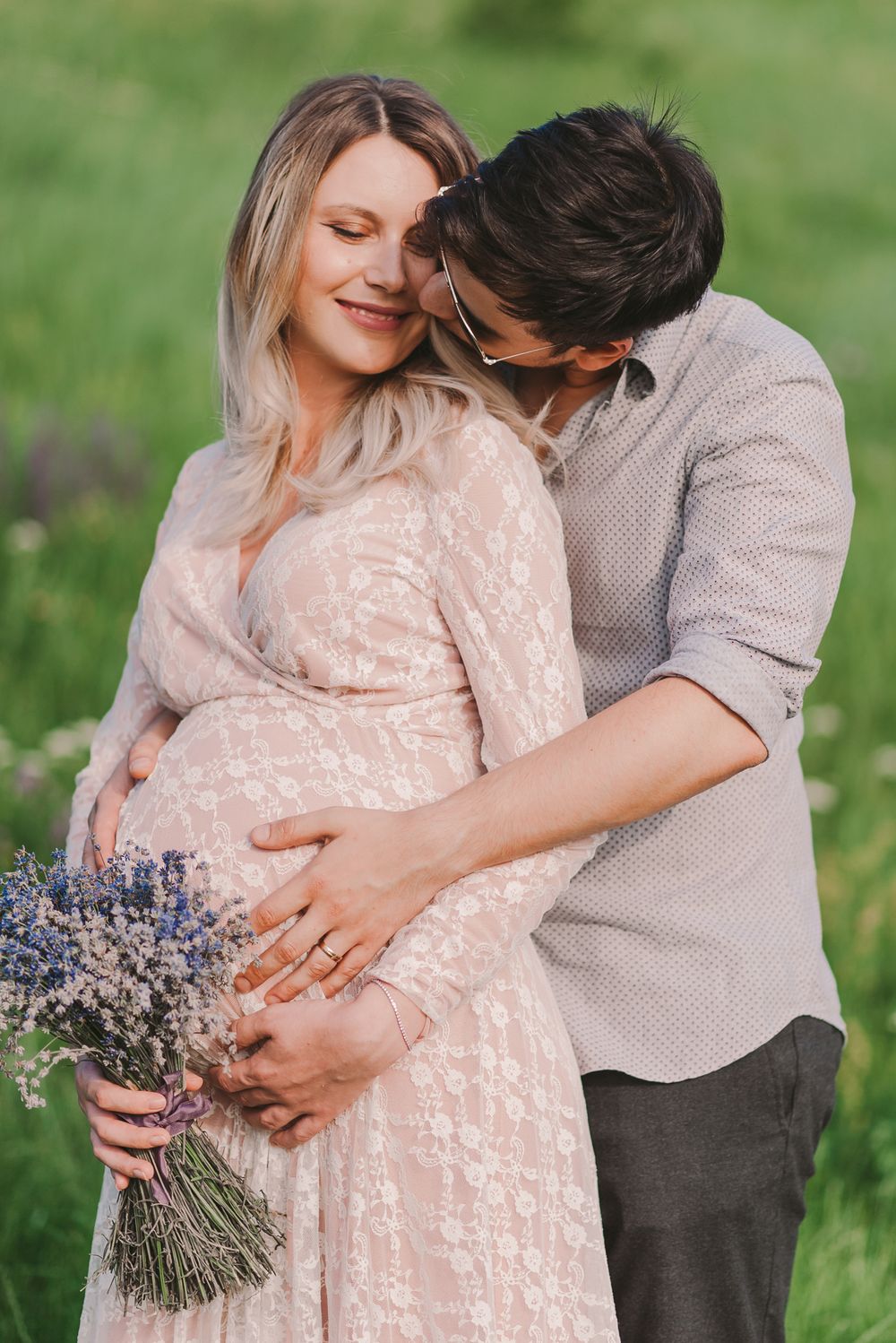 A couple embraces in a field while holding a bouquet of lavender flowers.