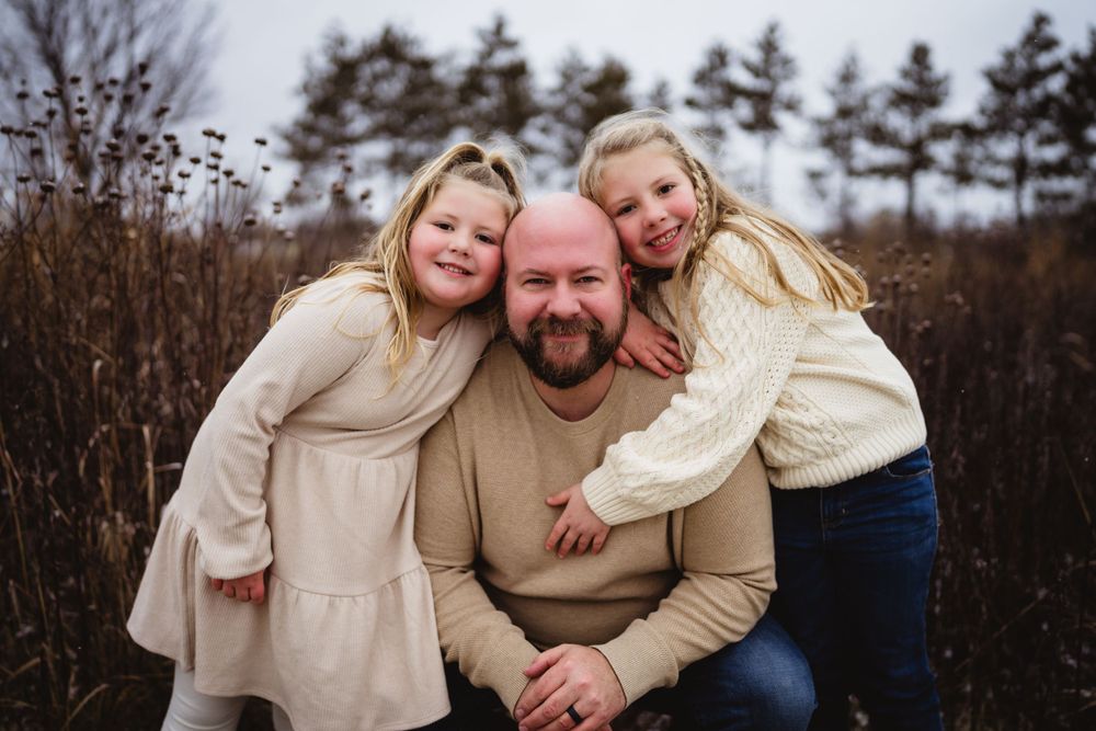 A heartwarming family portrait in a field with fall foliage and pine trees in the background.