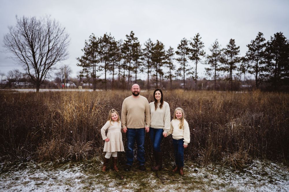 Family of four poses together in coordinating cream outfits against a winter landscape.