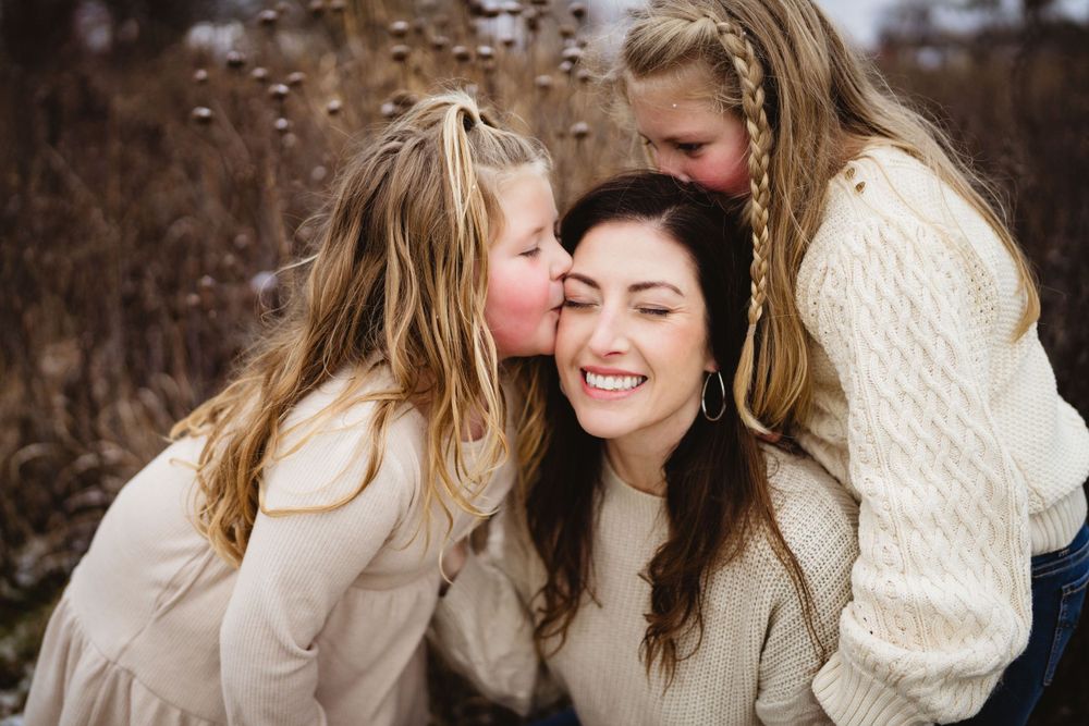 Three people share a joyful moment together outdoors in cream-colored sweaters.