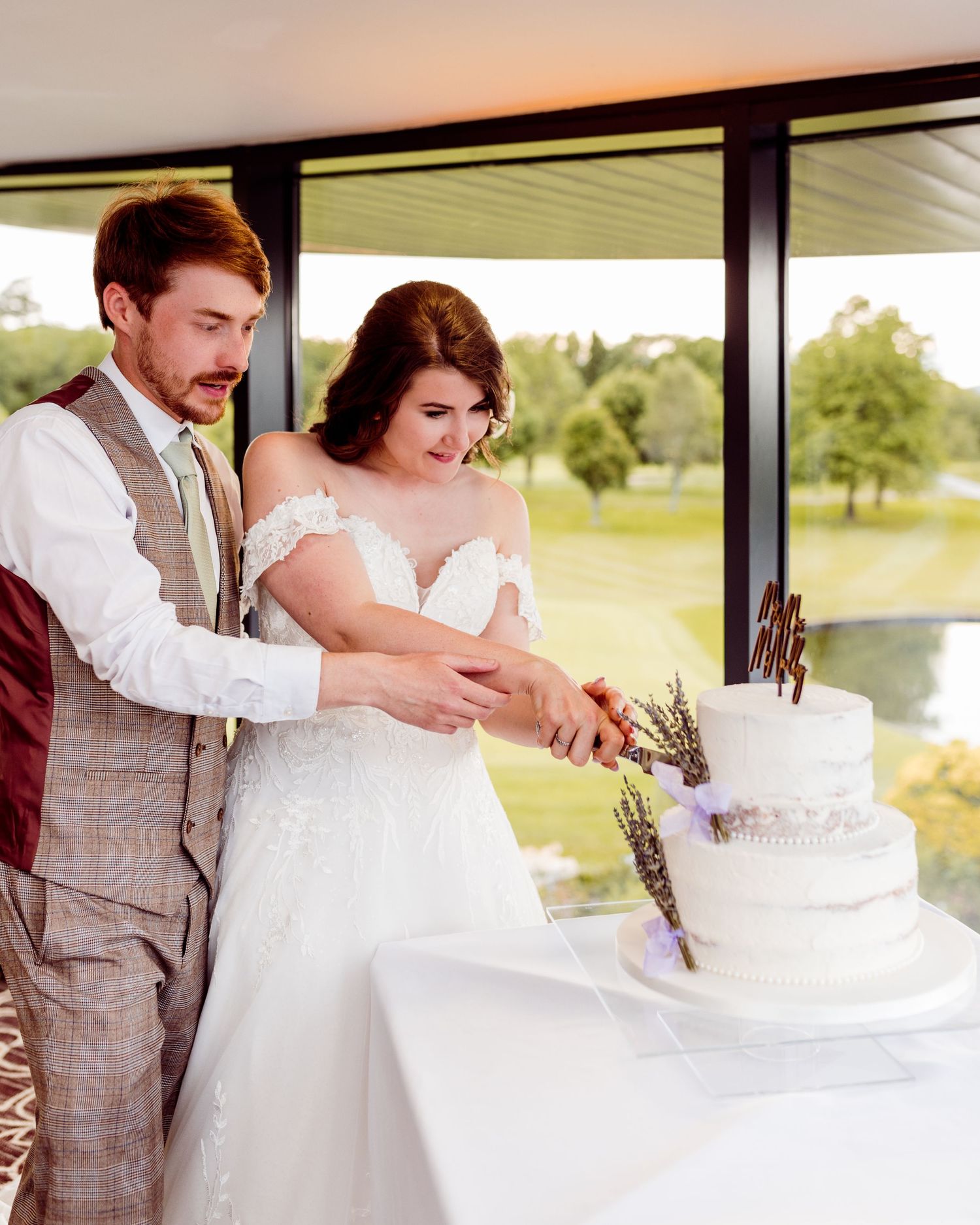 A bride and groom cut their elegant white wedding cake adorned with lavender sprigs during their reception.