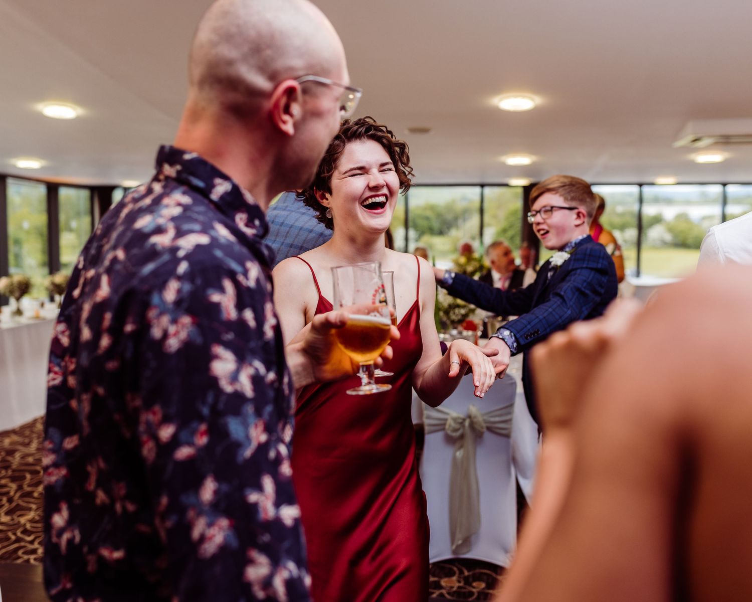 Wedding guests celebrating with drinks and laughter at an indoor reception venue.