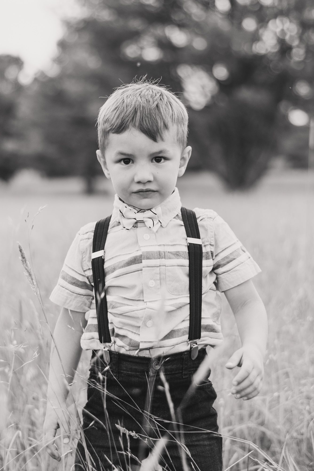 Little boy in suspenders with somber expression in field in black and white in Clarion Pennsylvania