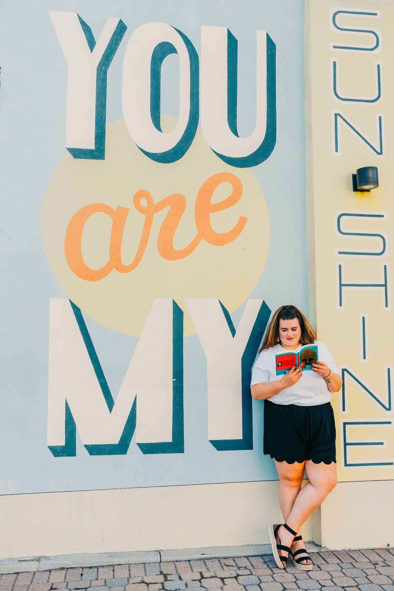Outdoor Headshot Session in St. Pete, FL; Woman posing with you are my sunshine mural
