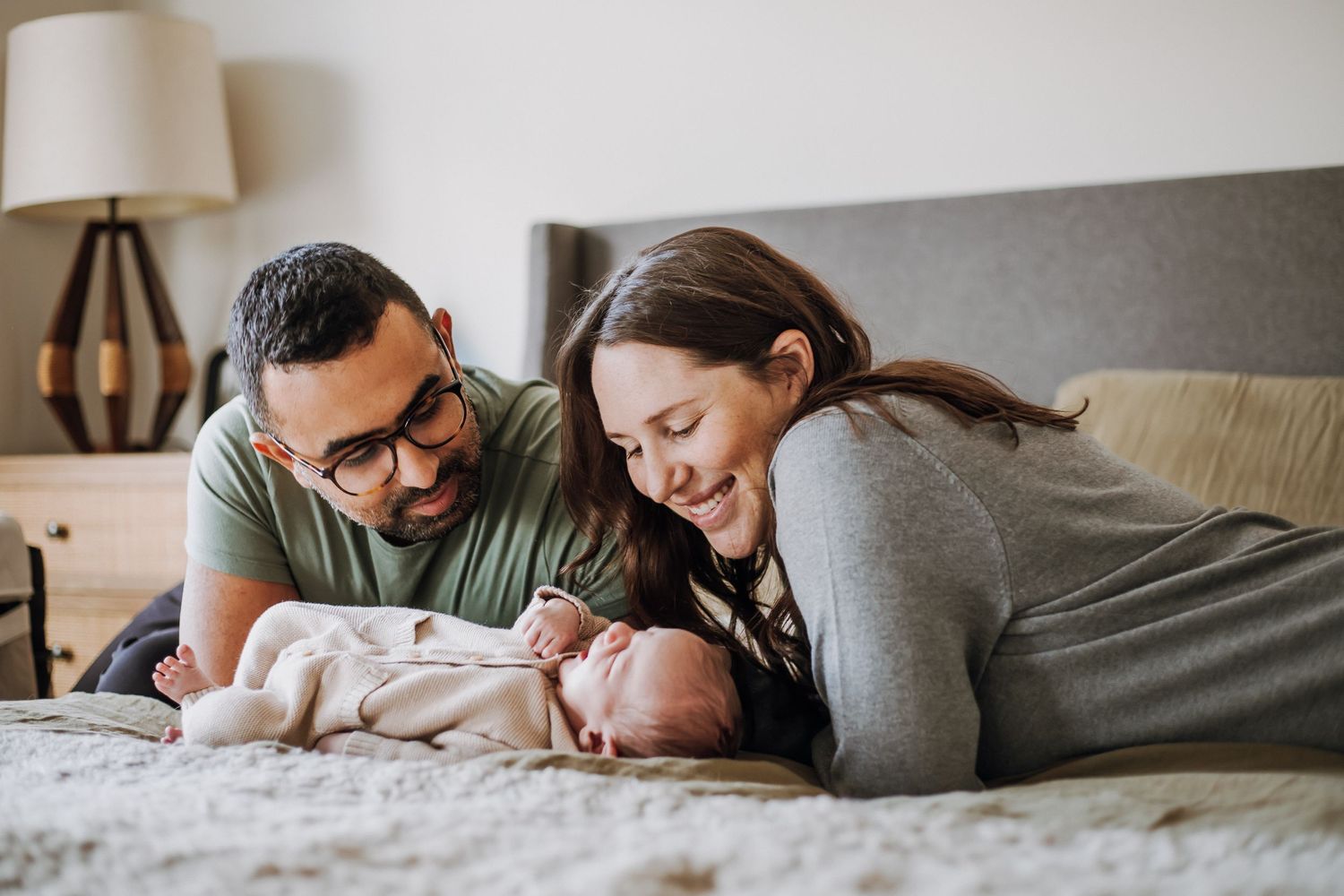 Parents lying on bed with newborn baby in cozy home setting.