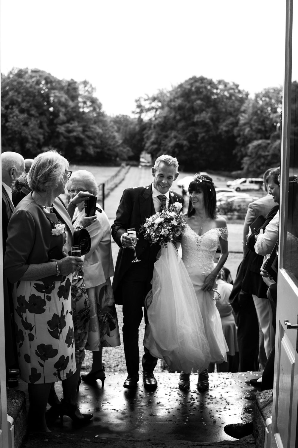 Wedding guests gathered outside on a rainy day holding champagne glasses.