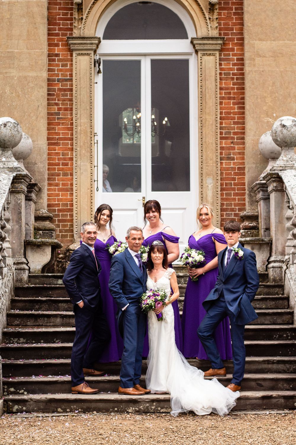 Wedding party posing on grand stone steps of historic mansion in formal attire.