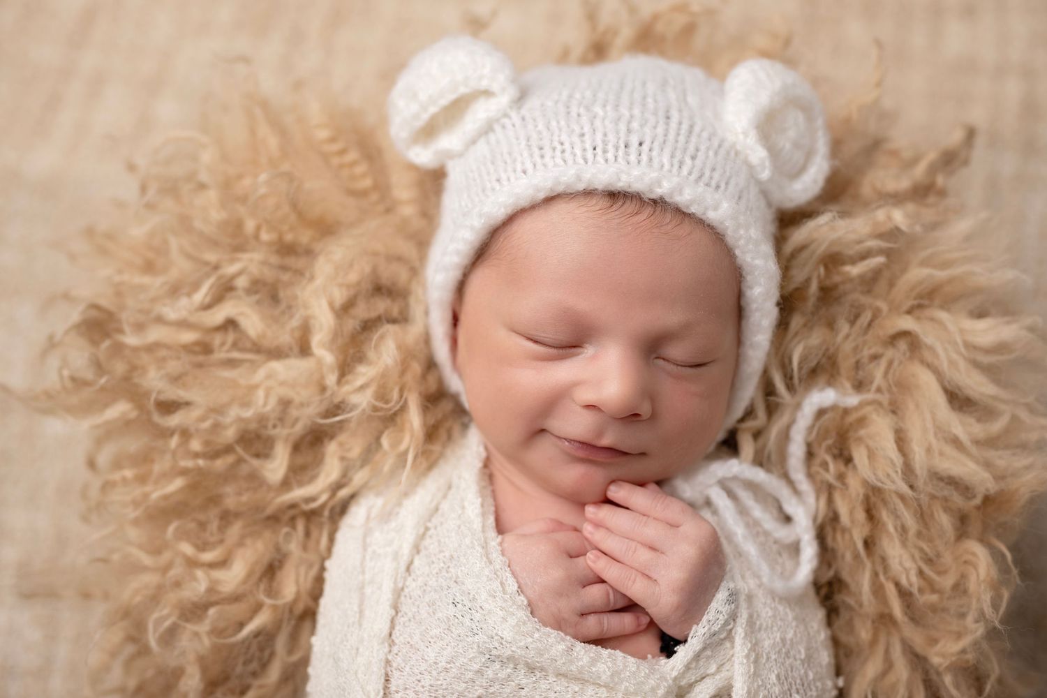 Newborn baby wearing a white knit hat sleeping peacefully on soft fur blanket.