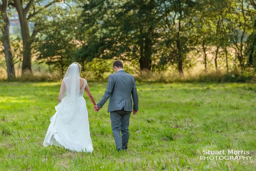 Bride and groom walk hand in hand in the meadow at west tower country house wedding venue.