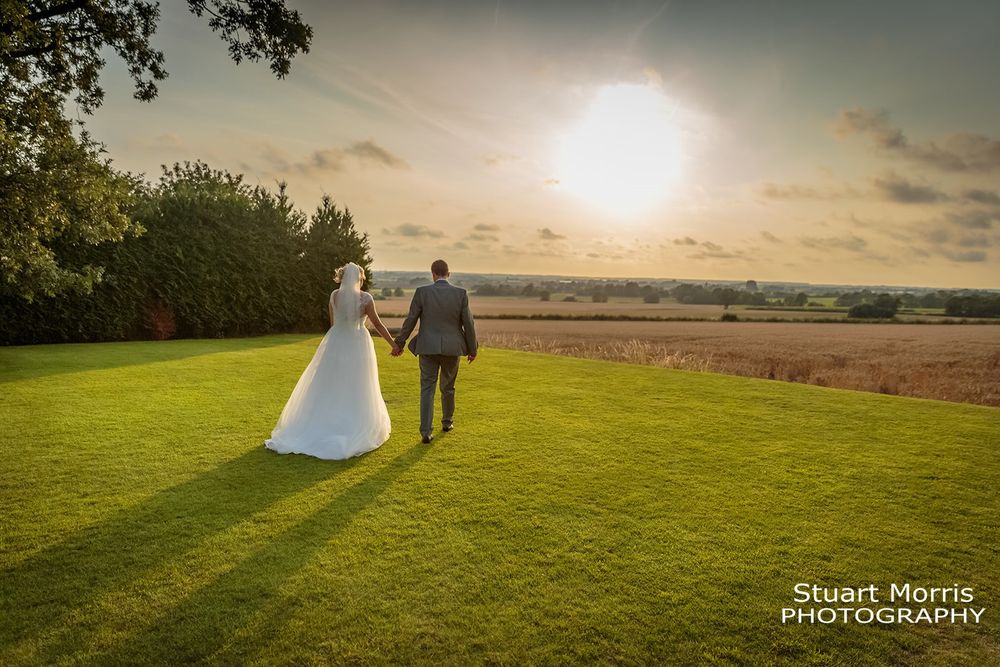 Bride and groom walk hand in hand in the grounds at west tower as the sun sets in the distance.