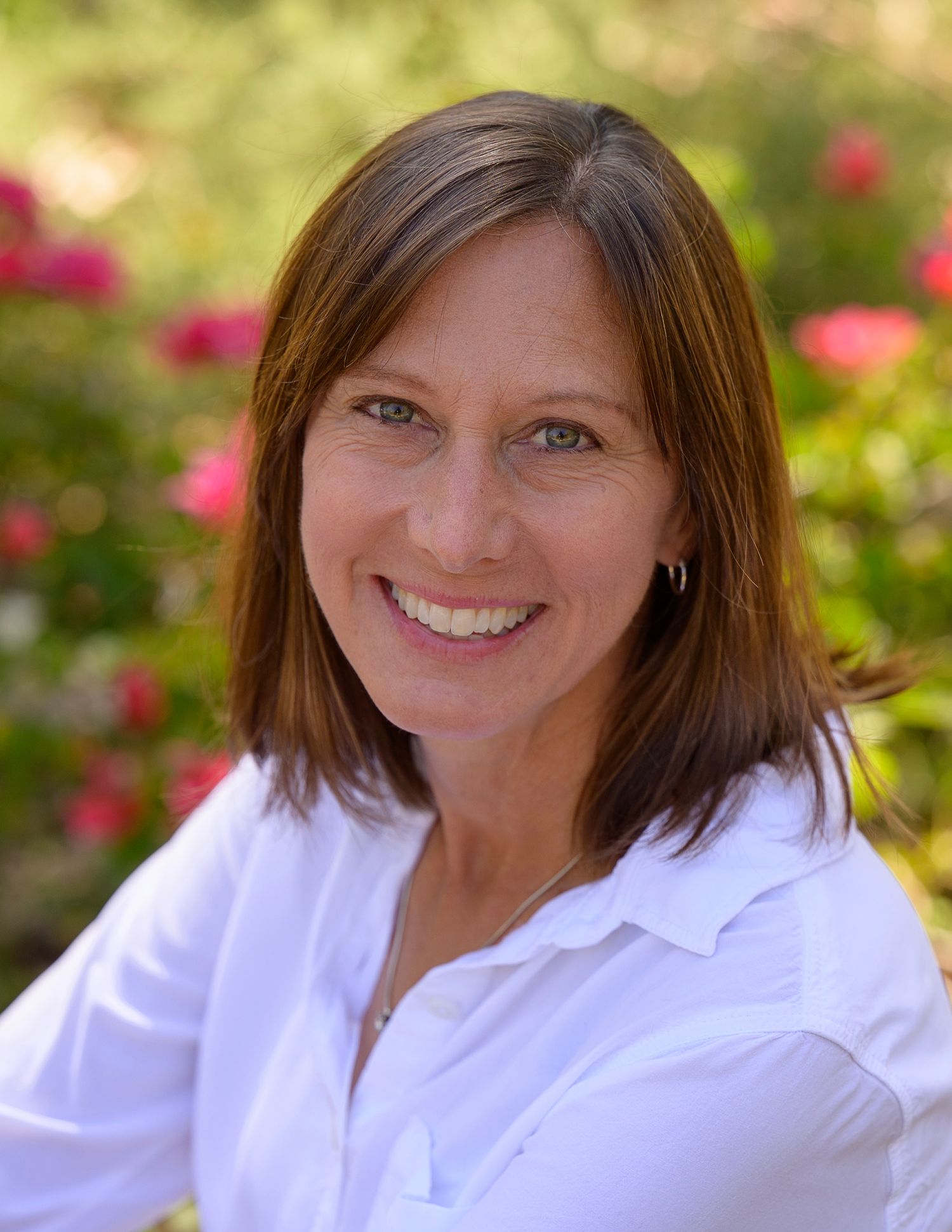 Professional headshot of woman in white shirt against pink floral garden background.