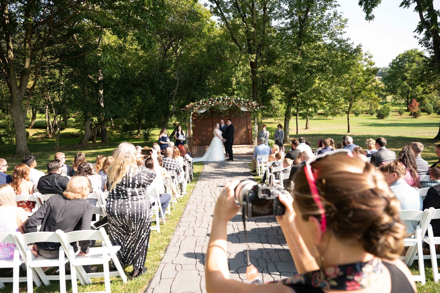 Wedding ceremony from photographer's perspective showing guests seated along brick path to arch.