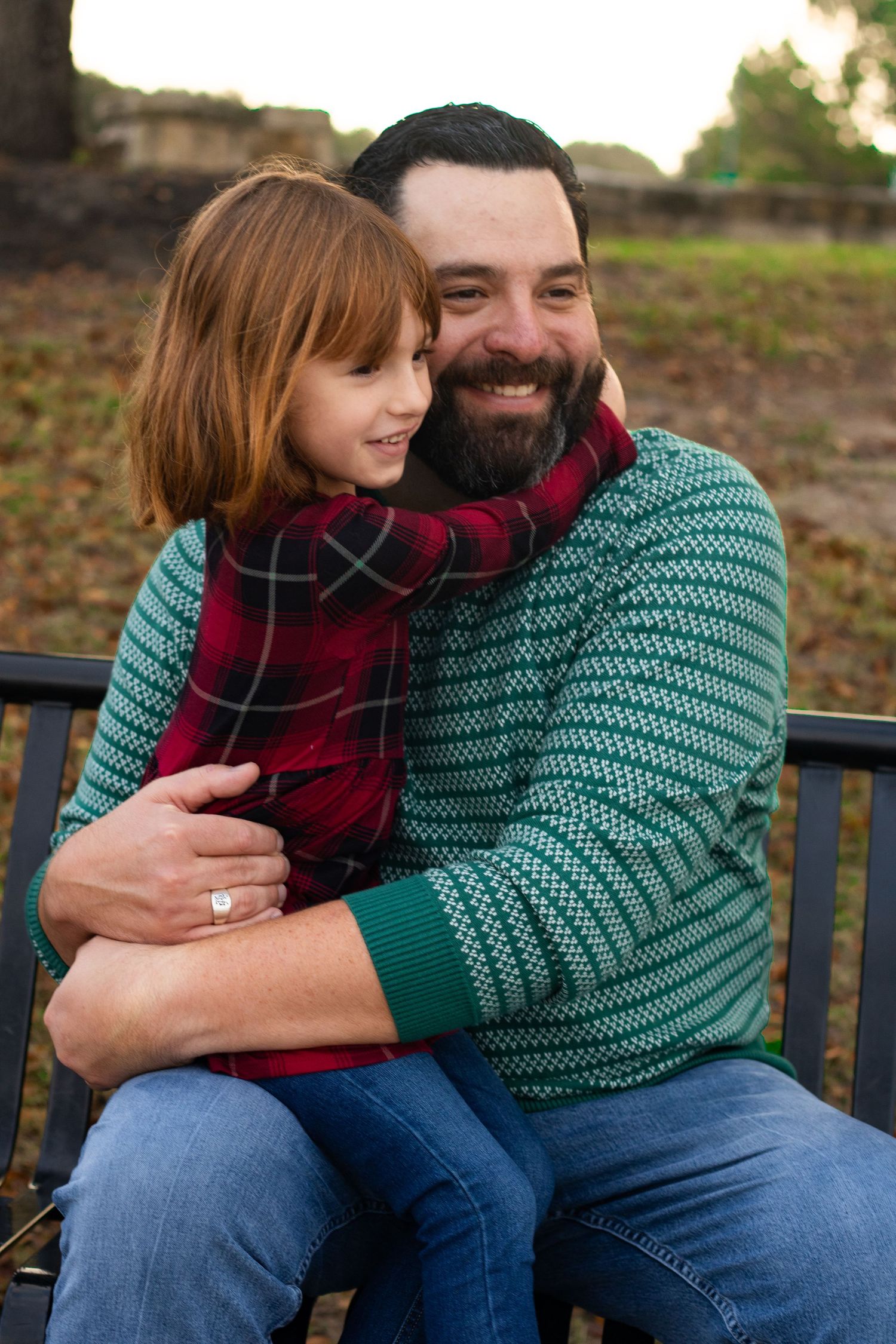 Parent and child share warm embrace while sitting on bench wearing cozy winter sweaters.