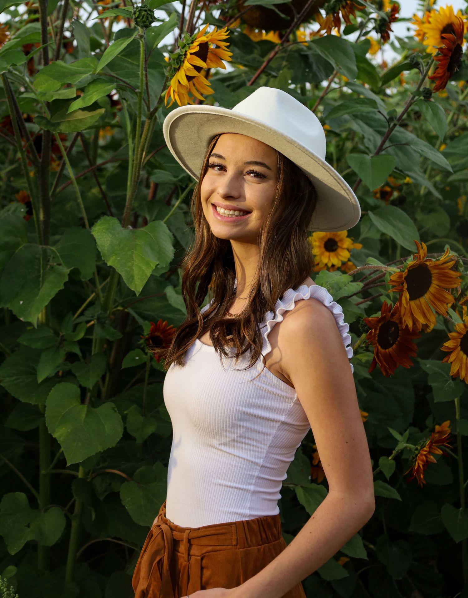 Summer portrait in a sunflower garden wearing a white sun hat and tank top.