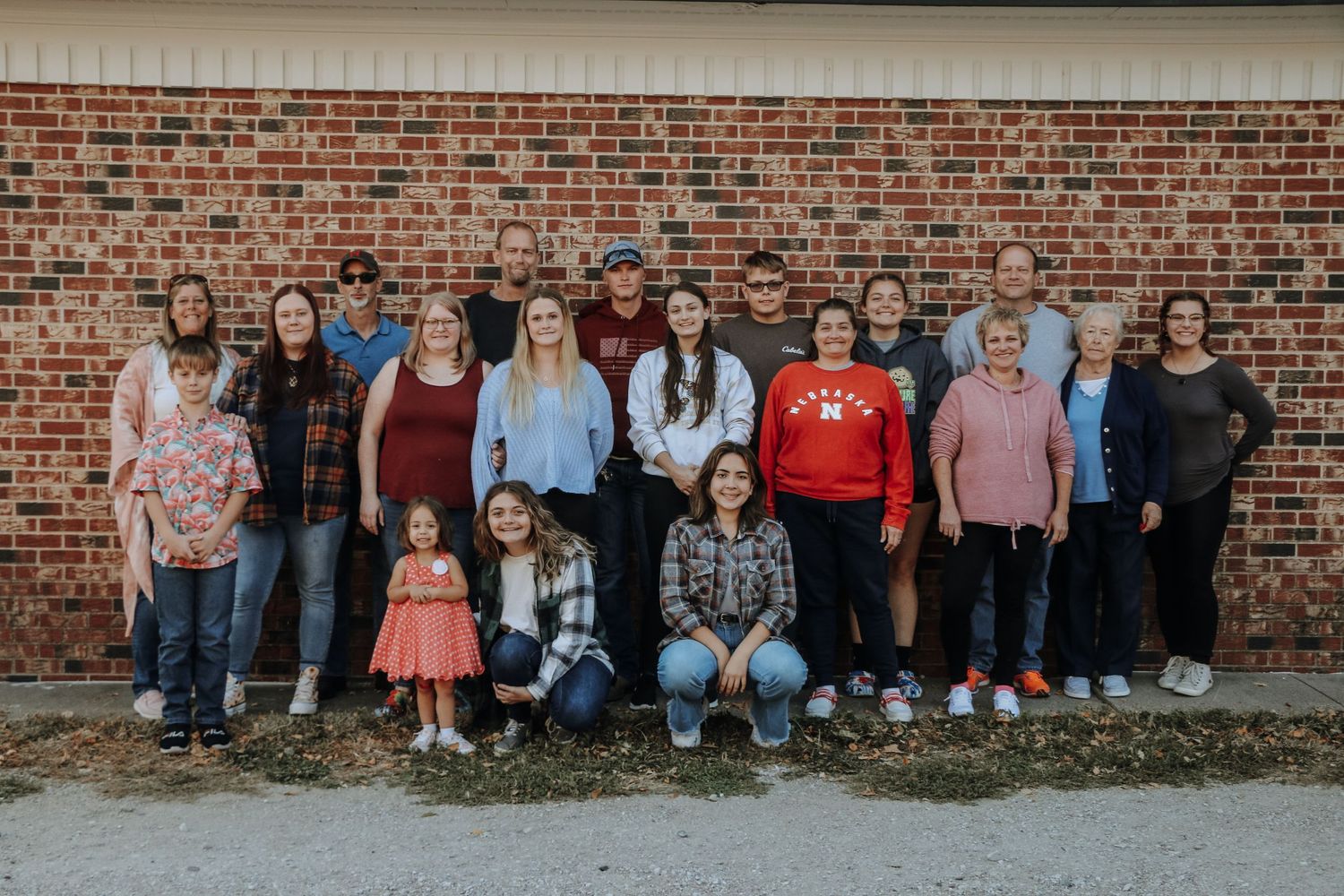 Large group portrait of extended family sitting against brick wall outdoors.