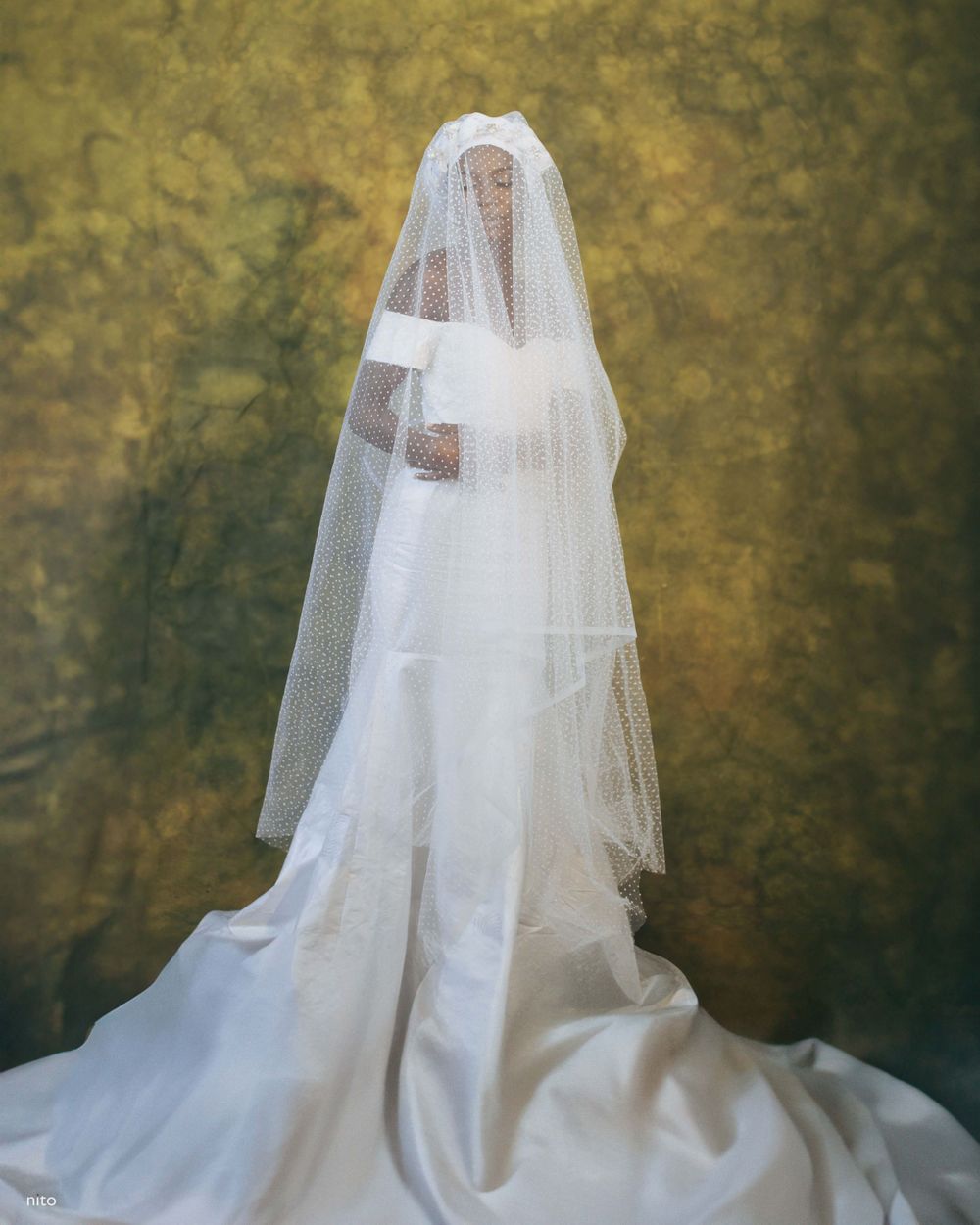 Back view of an elegant white wedding gown with flowing train and long veil against a textured gold background.