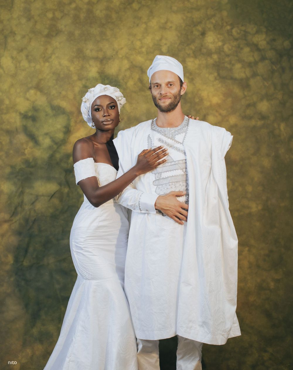 A couple in traditional white wedding attire posing together against a golden backdrop.
