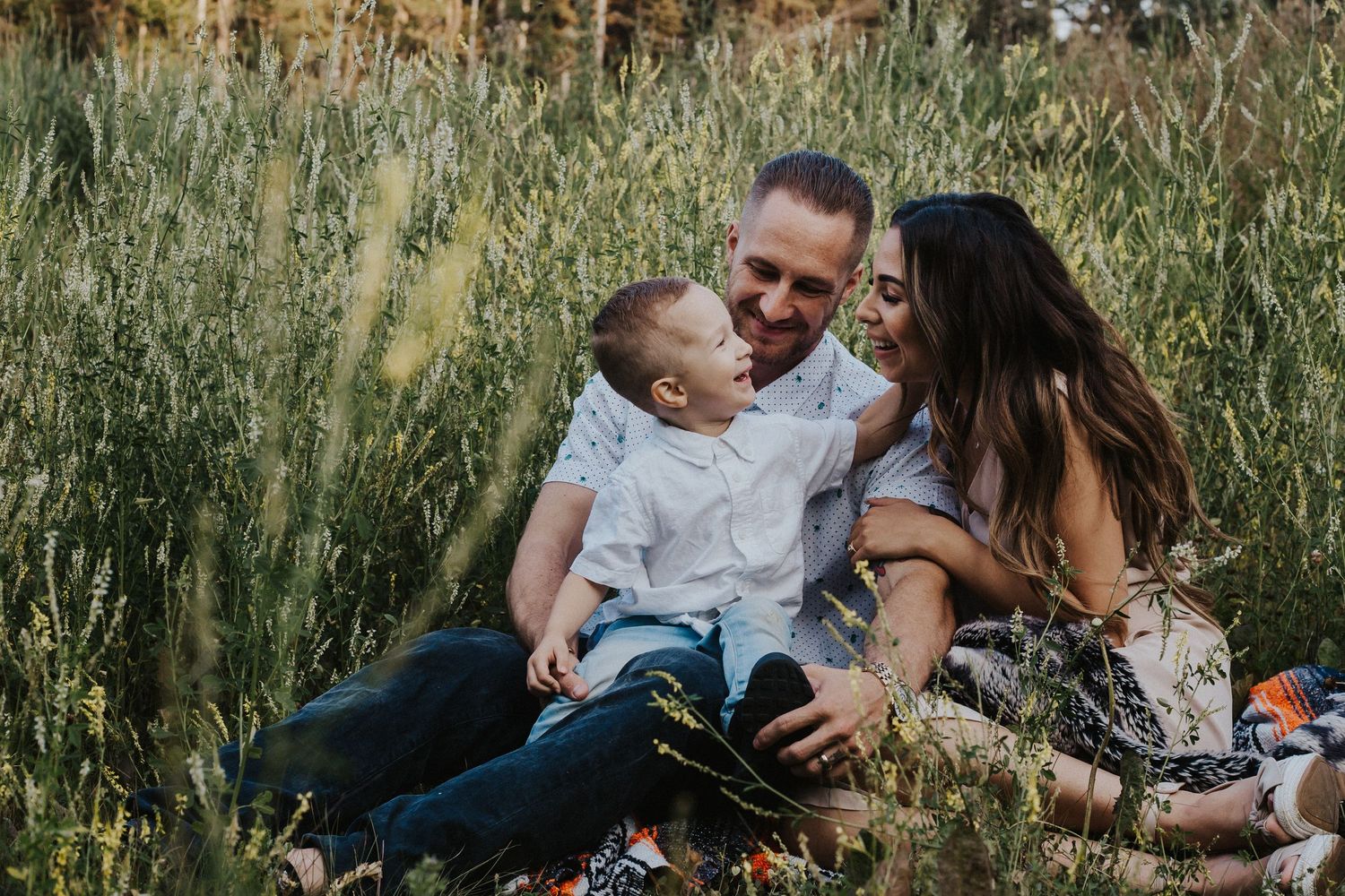 Family of three cuddling in a field of flowers while little boy touches his mother's face while laughing